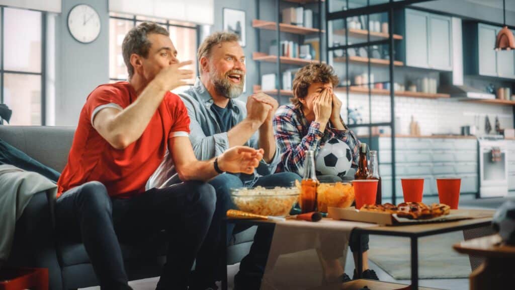 Three friends cheering while watching sports on tv